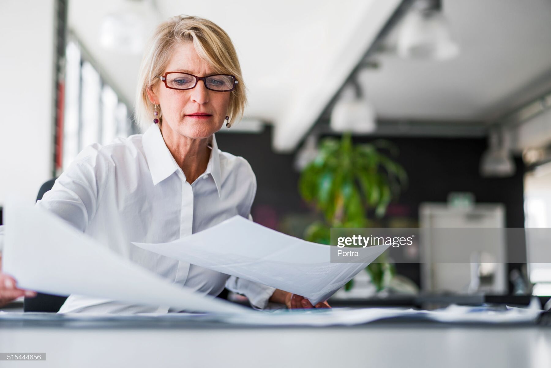 A photo of mature businesswoman examining documents at desk. Concentrated professional is analysing papers in office. Executive is in formals.