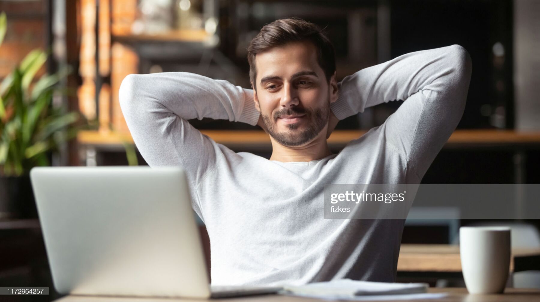 Caucasian businessman sitting at table in cafe modern cozy office looking at laptop screen feels satisfied proud with done work, serene man resting putting hands behind head relaxing no stress concept