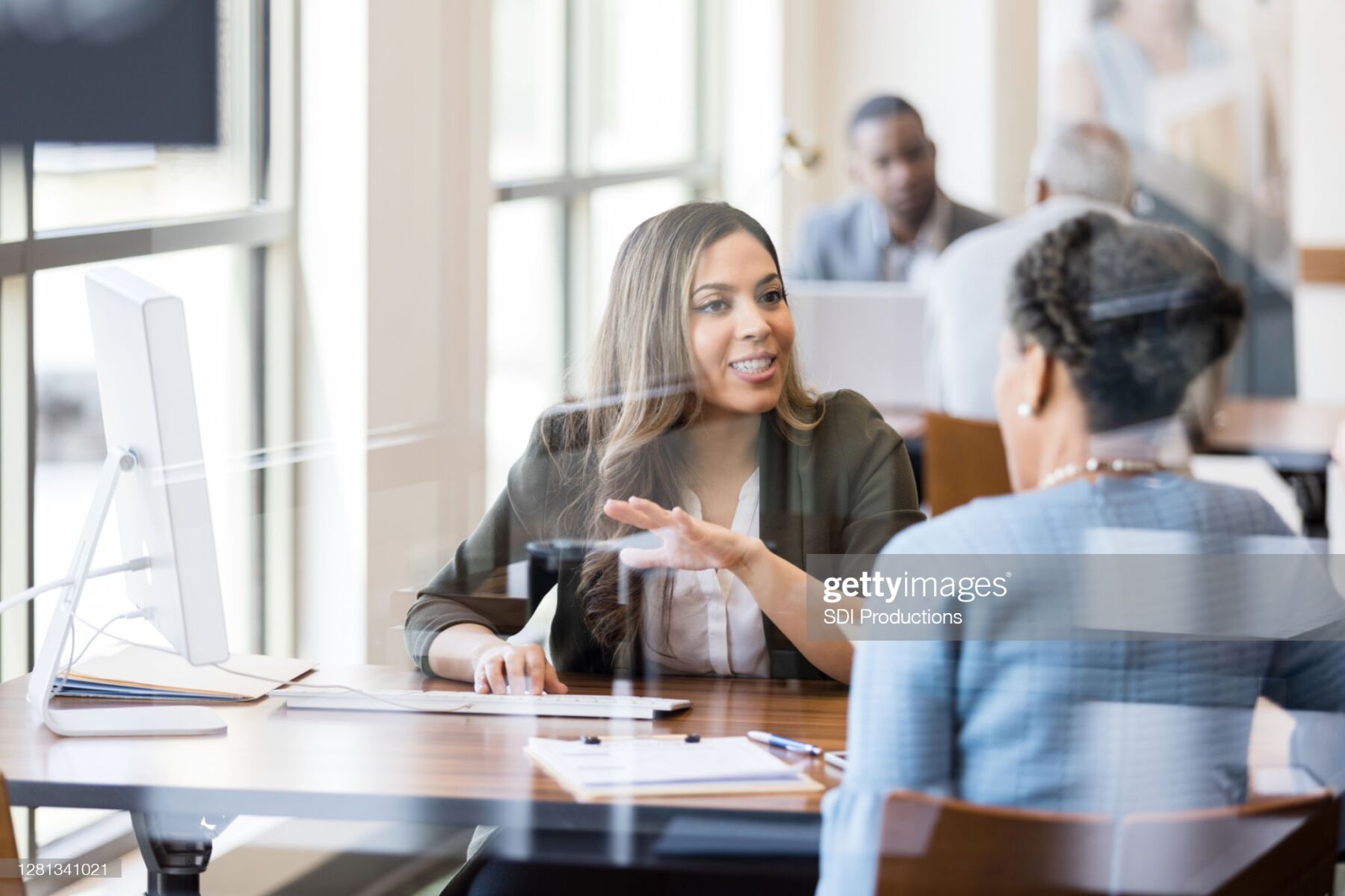A mid adult female bank employee gestures as she explains banking services to a female customer.